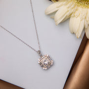 A sterling silver pendant chain with a central white stone surrounded by smaller white stones, displayed on a golden surface with a white flower in the background.